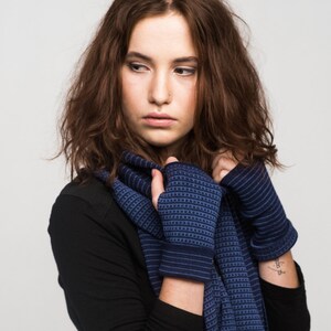Könnte beinhalten: Eine Frau trägt ein schwarzes Langarmshirt mit einem blau-weiß gestreiften Schal. Der Schal ist um ihren Hals gewickelt und vorne zu einem Knoten gebunden. Sie trägt auch blaue Fingerlose Handschuhe.