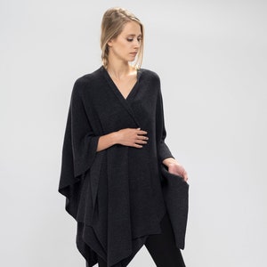 Op de afbeelding: Een antracietkleurige gebreide poncho met een gedrapeerd ontwerp. De poncho wordt gedragen over een zwarte legging en zwarte enkellaarsjes.