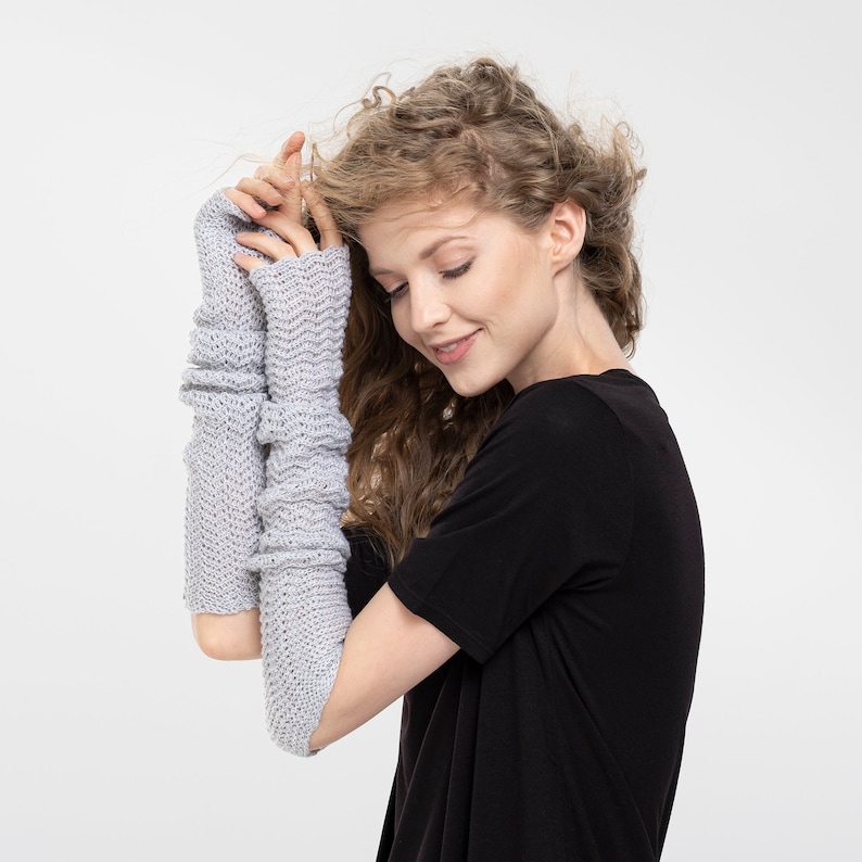 May include: A woman wearing a pair of gray fingerless gloves with a black t-shirt.