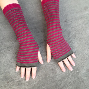 Könnte beinhalten: Ein Paar fingerlose Handschuhe mit einem gestreiften Muster in den Farben Pink und Grau.