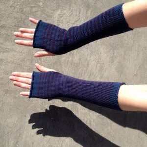 Könnte beinhalten: Ein Paar fingerlose Handschuhe in blau und burgunderrot gestreift. Die Handschuhe sind gestrickt und haben eine gerippte Struktur.
