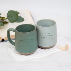 Op de afbeelding: Twee keramische mokken met handgeschreven berichten. De groene mok zegt "Grow old along with me? The best is yet to be." De blauwe mok zegt "In all the world, there is no love for me like yours. In all the world, there is no love for you like mine."