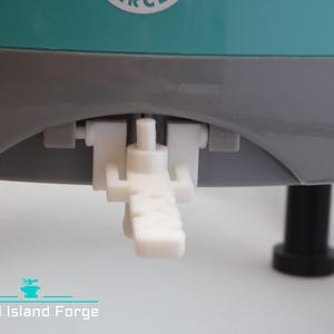 May include: A close-up of a white plastic lever attached to a grey and teal appliance. The lever is in the down position.