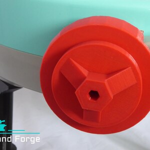 May include: A red plastic knob with a hexagonal center hole and three spokes. The knob is attached to a light blue and gray machine.