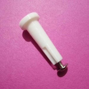 May include: A white plastic furniture component with a cylindrical body and a flat, circular head. The base features a small, silver-colored screw. The item is set against a pink background.