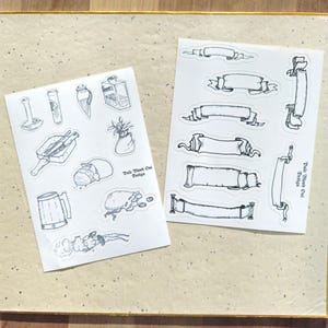 May include: Two sheets of stickers with black and white illustrations. One sheet features various medieval-themed items like a mug, a bag of coins, a bottle, and a plant. The other sheet features eight different banner designs. Both sheets have the text "Pale Wood Owl Design" printed on them.