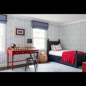 May include: A red wooden desk with drawers and a black chair sits in a room with blue and white chevron patterned wallpaper. A blue bed with a red blanket is in the background.