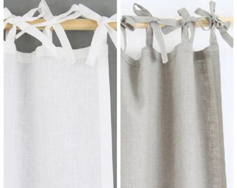 May include: Two linen curtain panels with tie-top headers. The panel on the left is white and the panel on the right is a light gray color. The text "CULTURED PEARL" is above the white panel and the text "ETERNAL SHORES" is above the gray panel.