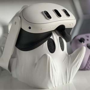 May include: White VR headset with a black strap and a white rhino-shaped stand. The headset has three sensors on the front.