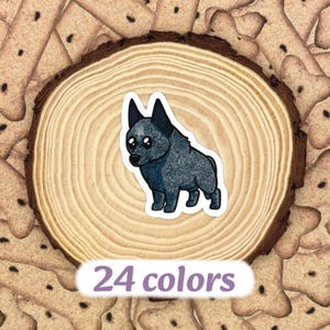 May include: A sticker featuring a cartoon-style blue heeler dog. The sticker is on a wooden slice with a bark edge, surrounded by dog biscuits. The text "24 colors" is at the bottom of the sticker.
