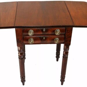 May include: A dark brown antique drop-leaf table with two drawers. The table has brass hardware and turned legs. The table's leaves are extended, and the overall design is classic and elegant.