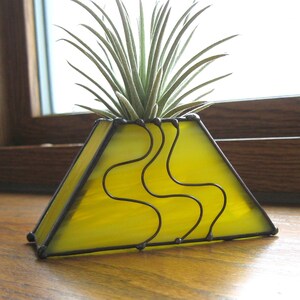 May include: A yellow stained glass triangular planter with a black wire design and an air plant inside.
