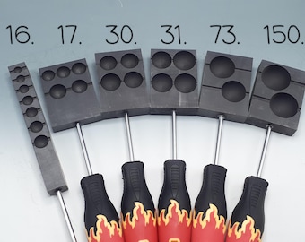 Puede incluir: Un juego de seis moldes de fundición de grafito gris oscuro con varias cavidades circulares, etiquetados 16, 17, 30, 31, 73 y 150. Cada molde está unido a una varilla de metal y un mango negro y rojo con un diseño gráfico de llamas amarillas.