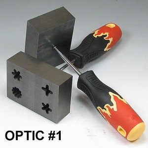 May include: Two gray graphite blocks with different shaped cutouts, one block has a star, a circle, and a plus sign cutout, the other block has a blank surface. A screwdriver with a black and red handle with a flame design is used to hold the blocks together. The text "OPTIC #1" is printed below the blocks.