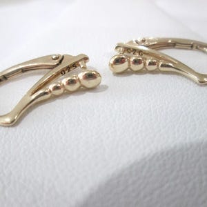 May include: A pair of gold-toned earrings with a curved design and a row of small beads. The earrings are marked "925" on one side and "926" on the other.