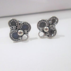 May include: A pair of silver earrings with a floral design. The earrings are made of silver and have a textured finish.
