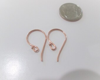 May include: Two rose gold earring hooks with a curved design and small ball accents. The hooks are displayed on a white surface next to a quarter coin for size comparison.