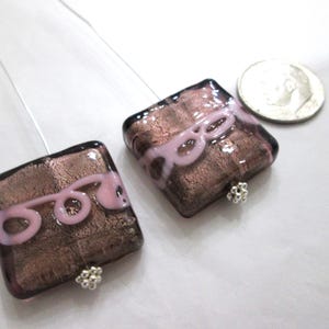 May include: Two square glass earrings with a brown and pink design. Each earring has a silver-colored post and a small silver-colored bead at the bottom. A dime is next to the earrings for size comparison.