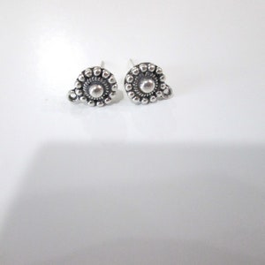 May include: A pair of silver stud earrings with a circular design featuring a central bead surrounded by smaller beads.