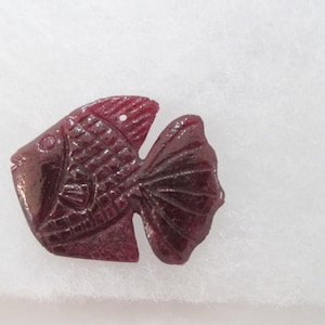 May include: A deep red glass fish pendant with a detailed design. The fish has a hole at the top for hanging.