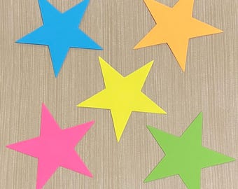 May include: Five paper stars in different colors: blue, orange, yellow, pink, and green. The stars are arranged in a semi-circle on a woodgrain background.