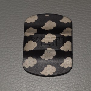 May include: A black accessory with a cloud pattern and the brand name "YETI" embossed on the front. The clouds are white and the background is black. The accessory is rectangular with rounded edges.