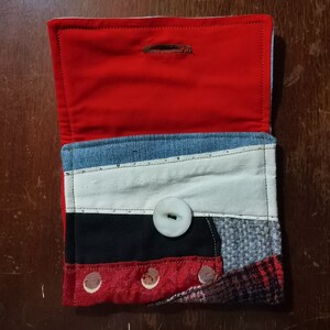 May include: A small red, white, black, and blue patchwork fabric wallet with a white button and a red lining.