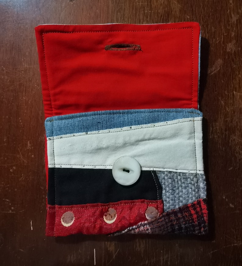 May include: A small red, white, black, and blue patchwork fabric wallet with a white button and a red lining.