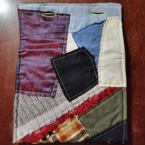 K&ouml;nnte beinhalten: Ein Patchwork-Deckenst&uuml;ck mit verschiedenen Stoffen in Rot-, Blau-, Gr&uuml;n- und Braunt&ouml;nen. Die Decke besteht aus verschiedenen Texturen und Mustern, darunter Karos, Blumen und einfarbige Stoffe. Die Decke ist mit einem leuchtend gelben Faden zusammengen&auml;ht.