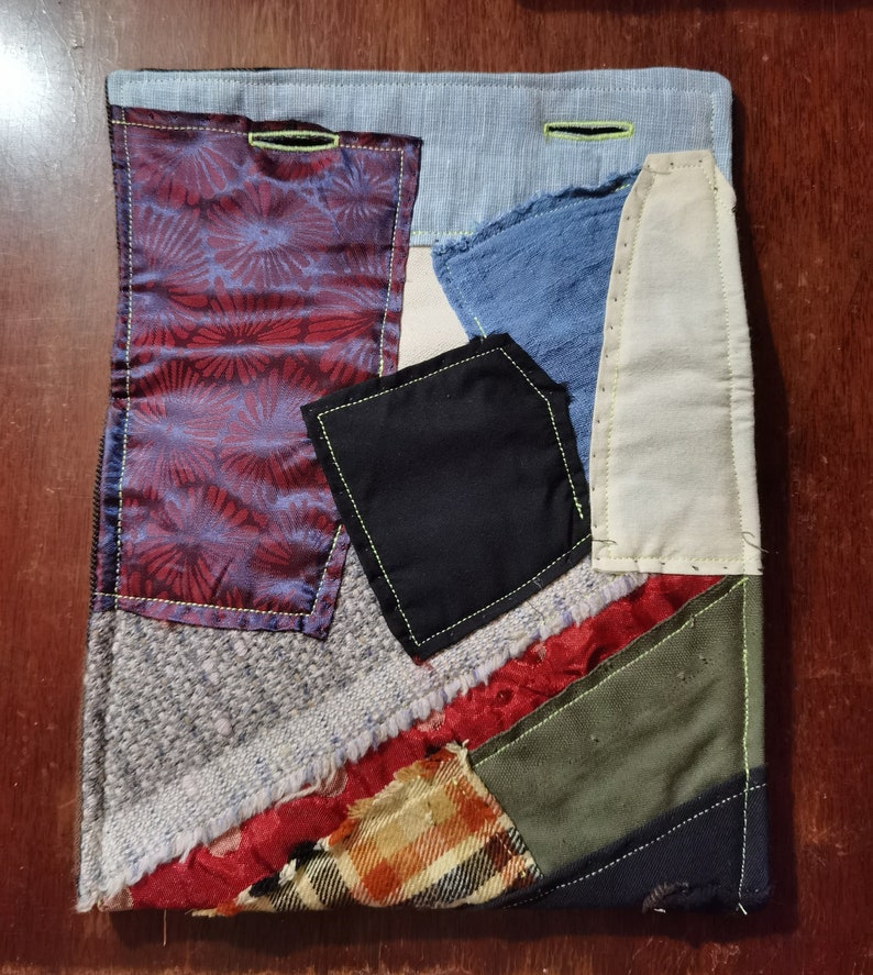 K&ouml;nnte beinhalten: Ein Patchwork-Deckenst&uuml;ck mit verschiedenen Stoffen in Rot-, Blau-, Gr&uuml;n- und Braunt&ouml;nen. Die Decke besteht aus verschiedenen Texturen und Mustern, darunter Karos, Blumen und einfarbige Stoffe. Die Decke ist mit einem leuchtend gelben Faden zusammengen&auml;ht.