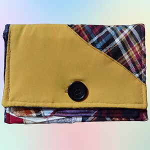 May include: A yellow fabric clutch with a plaid fabric flap and a black button. The clutch is made of a patchwork of different fabrics.