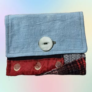 May include: A small blue fabric wallet with a white button and a red, black, and gray patchwork flap.