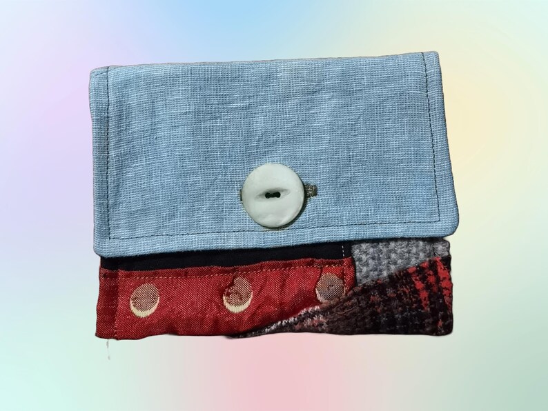 May include: A small blue fabric wallet with a white button and a red, black, and gray patchwork flap.