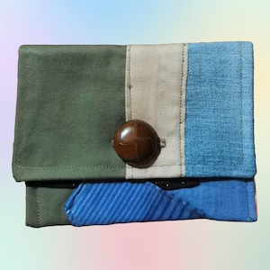 May include: A small, rectangular wallet made of different fabrics. The wallet has a green, beige, and blue patchwork design with a brown button.