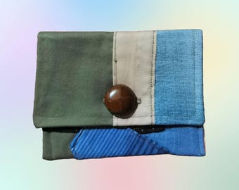May include: A small, rectangular wallet made of different fabrics. The wallet has a green, beige, and blue patchwork design with a brown button.