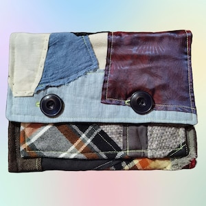 Puede incluir: Una cartera de tela de patchwork con un diseño de cuadros azules, blancos y marrones. La cartera tiene dos botones grandes y un cierre de solapa.