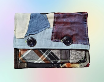 May include: A patchwork fabric wallet with a blue, white, and brown plaid design. The wallet has two large buttons and a flap closure.