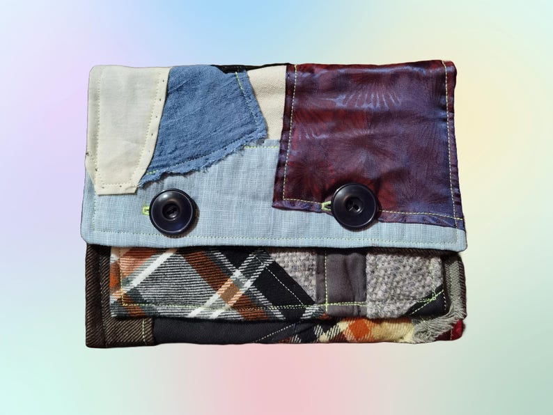 K&ouml;nnte beinhalten: Eine Patchwork-Geldb&ouml;rse aus Stoff mit einem blau-wei&szlig;-braunen Karomuster. Die Geldb&ouml;rse hat zwei gro&szlig;e Kn&ouml;pfe und einen Klappverschluss.