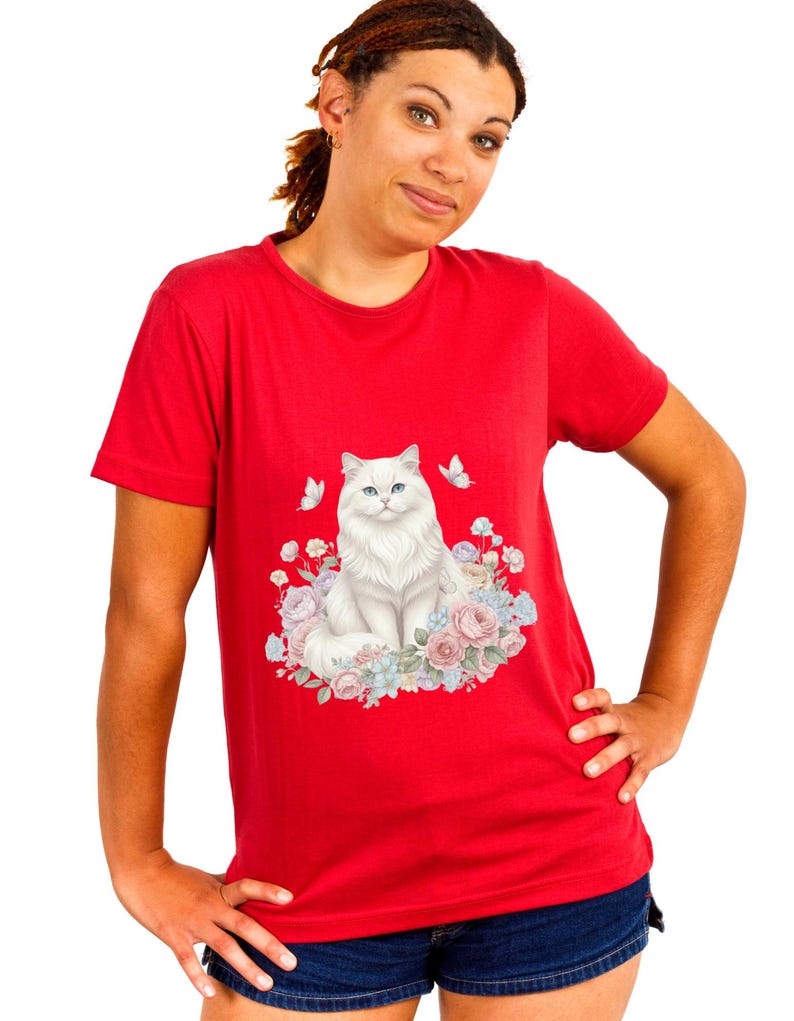 May include: A red t-shirt with a graphic of a white cat with blue eyes, encircled by pastel flowers and butterflies. The design is centered on the shirt, with a bright red backdrop.