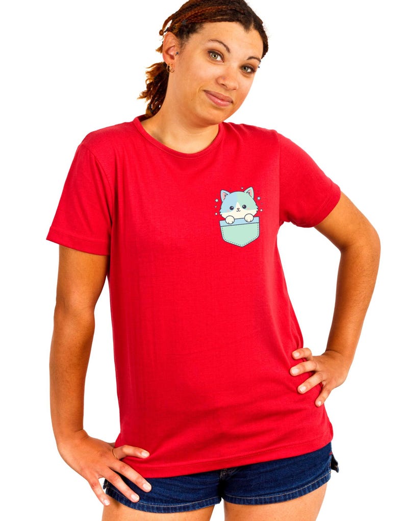 K&ouml;nnte beinhalten: Rotes T-Shirt mit einer Tasche mit einem Cartoon-Katzen-Design. Die Katze hat blaues und gr&uuml;nes Fell und schaut aus einer hellblauen Tasche heraus. Das Shirt hat eine einfarbige rote Farbe.