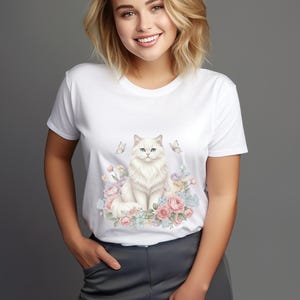 May include: White t-shirt with a watercolour illustration of a fluffy white cat with blue eyes, surrounded by pink and blue flowers and butterflies. The design creates a whimsical and artistic aesthetic.