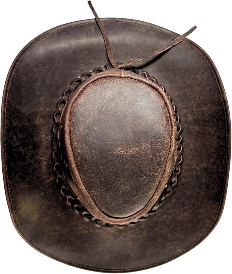 Pode incluir: Chap&eacute;u de cowboy de couro castanho escuro com aba larga e faixa tran&ccedil;ada ao redor da coroa. O chap&eacute;u tem um acabamento desgastado e uma gravata de couro. Este chap&eacute;u de estilo ocidental &eacute; perfeito para atividades ao ar livre.