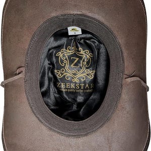 Pode incluir: Chap&eacute;u de couro castanho com aba larga, visto por dentro. O interior apresenta um forro de cetim preto com o logotipo "ZEEKSTAR" e um emblema dourado. O chap&eacute;u &eacute; de tamanho m&eacute;dio.