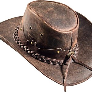 Pode incluir: Um chap&eacute;u de cowboy de couro castanho com aba larga e faixa tran&ccedil;ada. O chap&eacute;u apresenta detalhes met&aacute;licos decorativos e uma fita de couro. Um acess&oacute;rio cl&aacute;ssico de estilo ocidental.