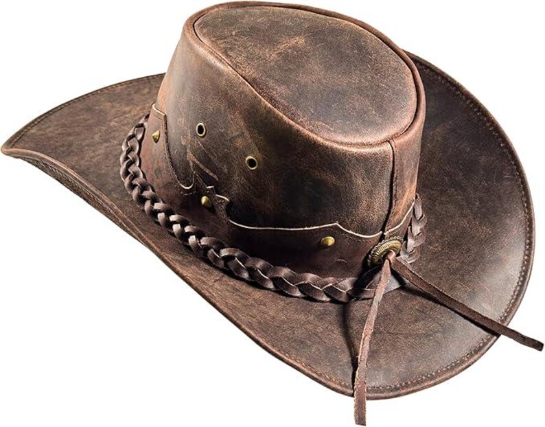 Pode incluir: Um chap&eacute;u de cowboy de couro castanho com aba larga e faixa tran&ccedil;ada. O chap&eacute;u apresenta detalhes met&aacute;licos decorativos e uma fita de couro. Um acess&oacute;rio cl&aacute;ssico de estilo ocidental.