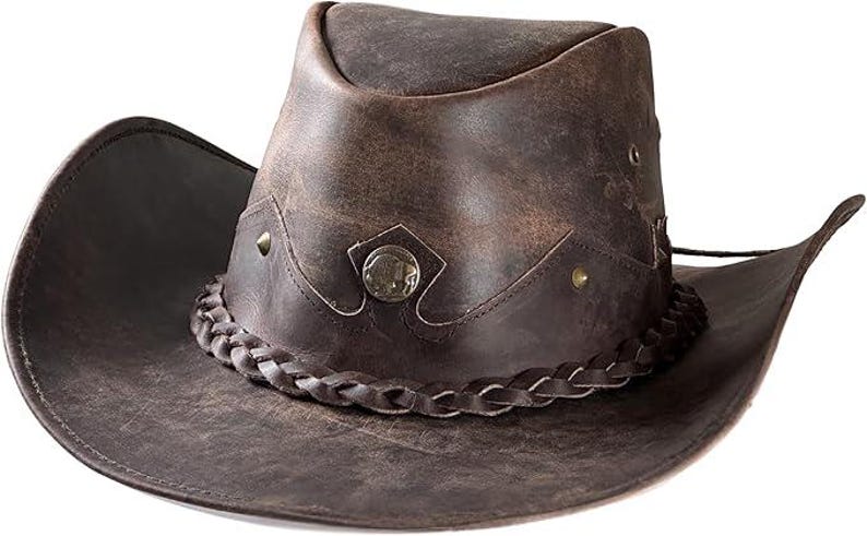 Pode incluir: Chap&eacute;u de cowboy de couro castanho desgastado com uma faixa tran&ccedil;ada e detalhes met&aacute;licos decorativos. O chap&eacute;u apresenta uma aba larga e um design ocidental cl&aacute;ssico, ideal para atividades ao ar livre ou eventos &agrave; fantasia.