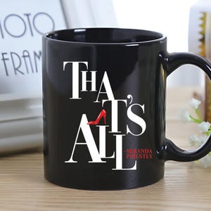 May include: Black ceramic mug with the text "That's All" in white, featuring a red high heel shoe graphic. The mug also includes the text "-Miranda Priestly".
