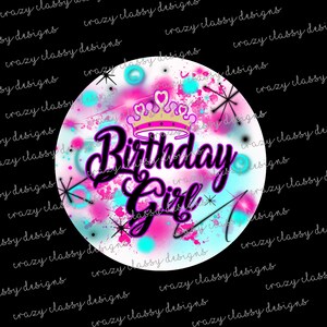 Pode incluir: Um círculo branco com um design de tinta salpicada rosa, azul e branca. As palavras "Birthday Girl" são escritas em preto com um contorno rosa. Uma coroa dourada com corações rosa está acima das palavras.