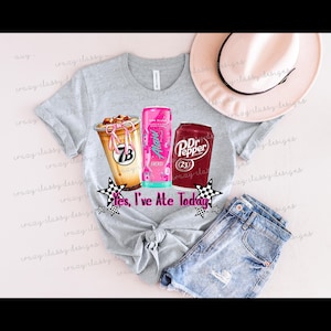 May include: A light gray t-shirt with a graphic of a coffee drink, an energy drink, and a Dr. Pepper can. The text "Yes, I've Ate Today" is below the graphics. A pair of denim shorts and a hat are also in the image.