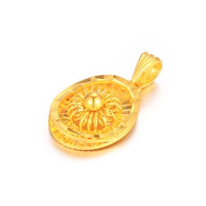 Puede incluir: Un colgante dorado con forma ovalada. El colgante presenta un diseño floral central con un centro esférico y pétalos en espiral. El colgante tiene una superficie texturizada y un lazo para una cadena.